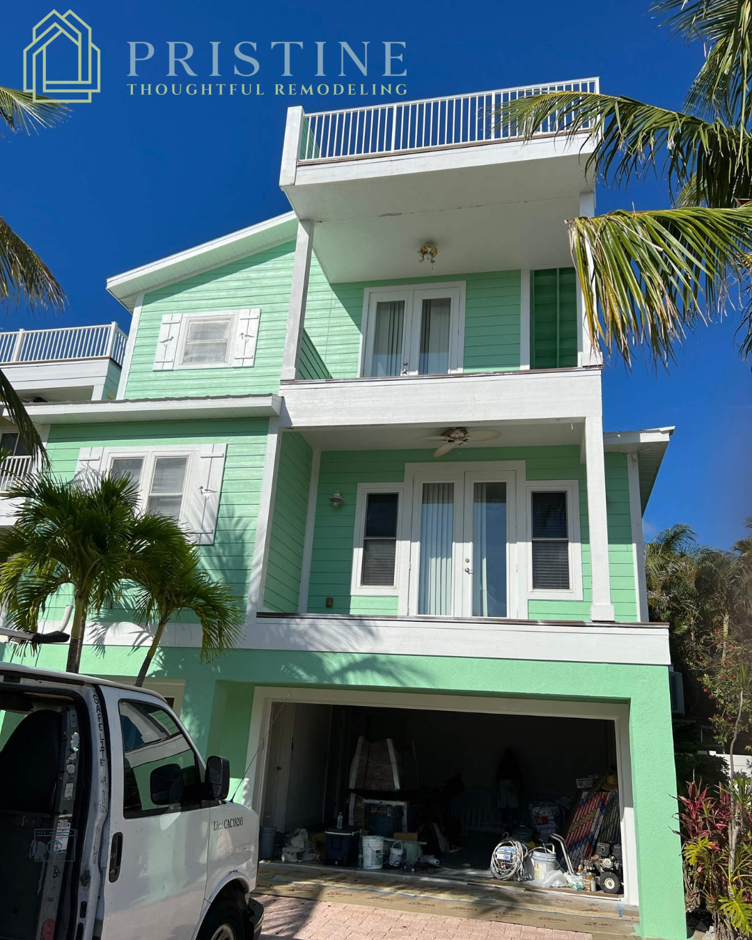 Mint-green three-story house with a balcony, garage, and parked van under a clear blue sky