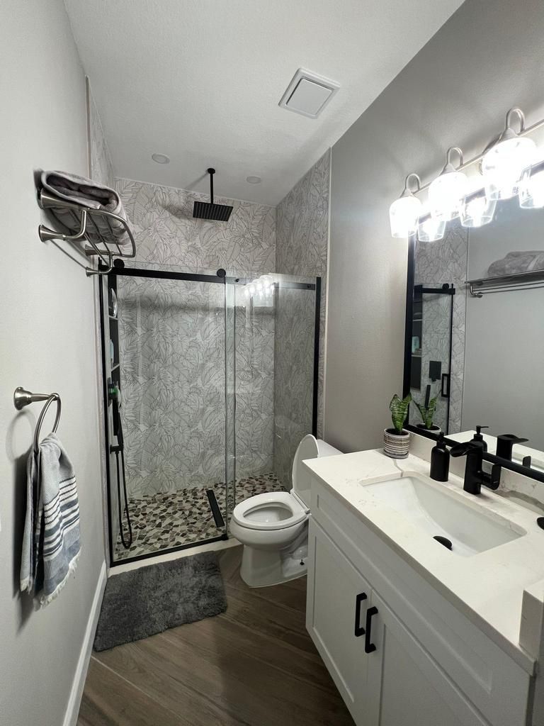 Narrow modern bathroom with glass shower, toilet, and vanity sink with lit mirror.