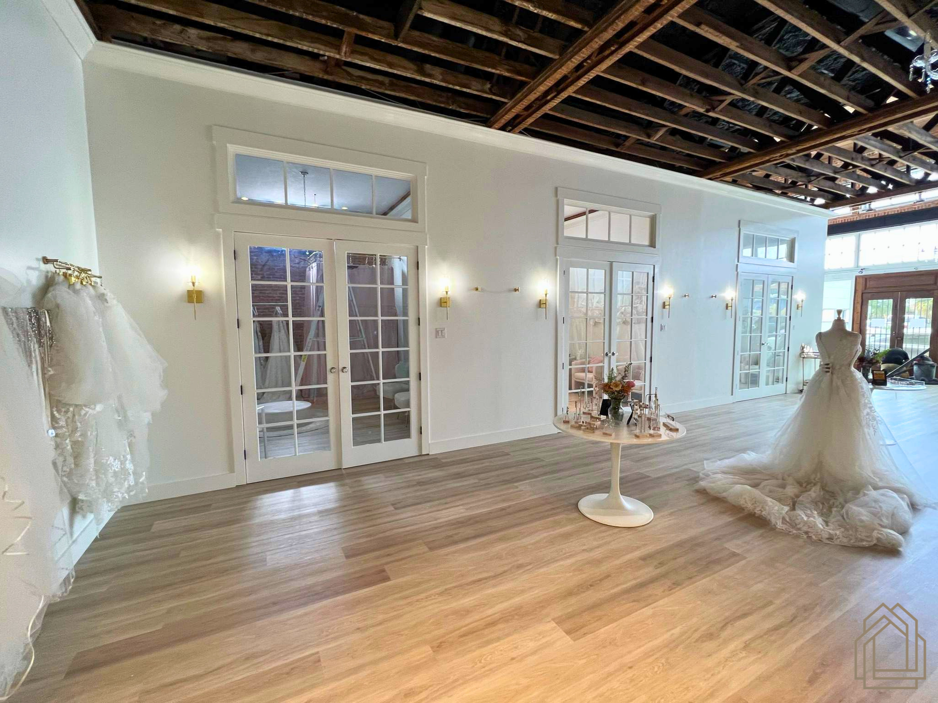 Bridal shop interior with wedding dresses, hardwood floors, and large French doors in a bright studio