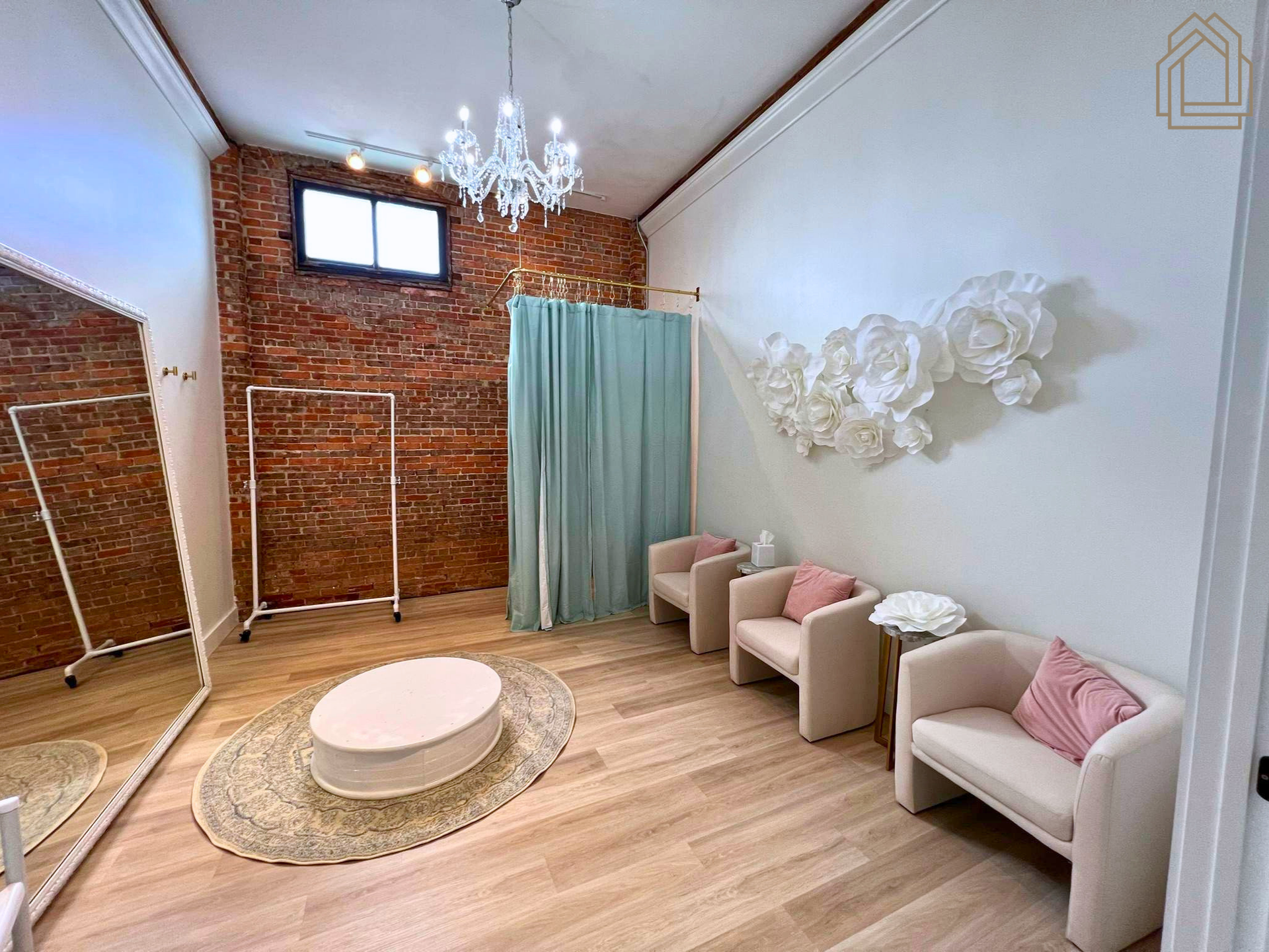 Bright living room with exposed brick walls, white chairs, a round rug, chandelier, and teal curtains