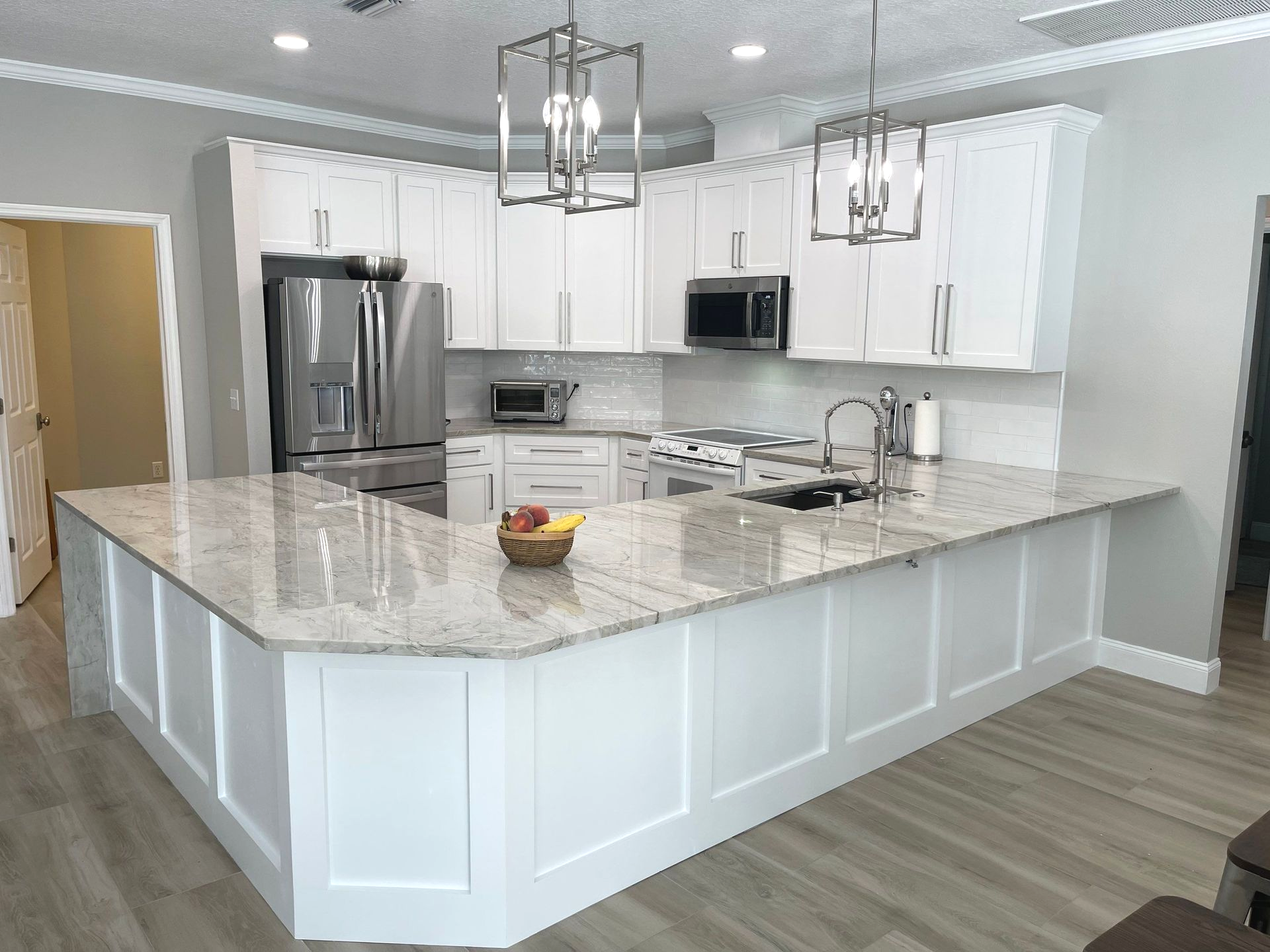 Modern white kitchen with a large marble island, stainless steel appliances, and pendant lights.