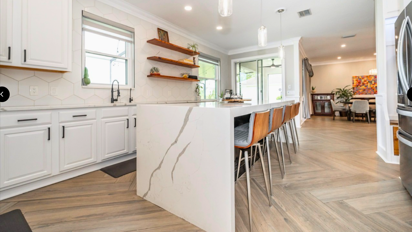 Bright modern kitchen with white cabinets, marble island, and orange bar stools in an open-plan home