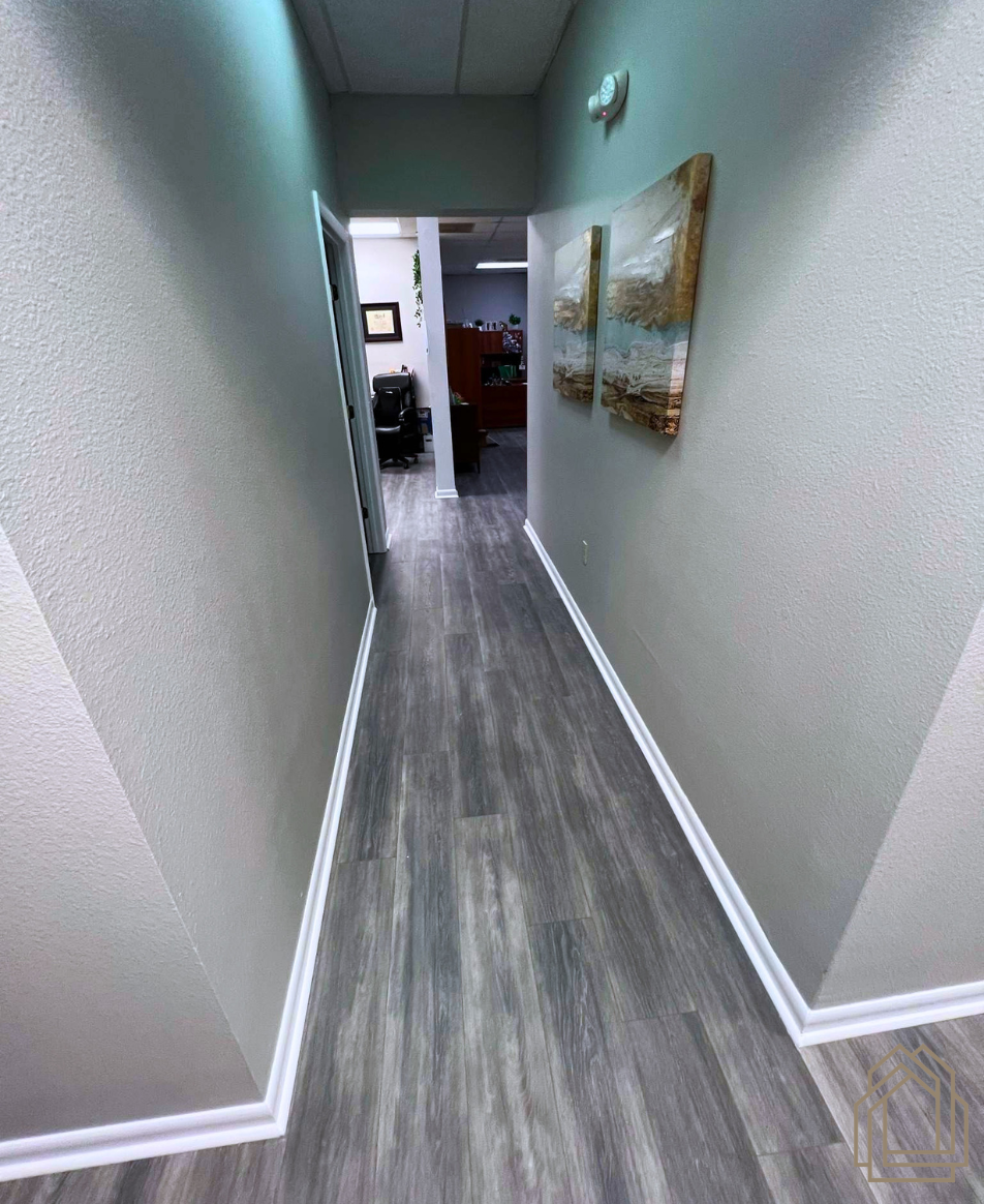 Narrow hallway with gray wood floor, white walls, and a framed painting on the right.