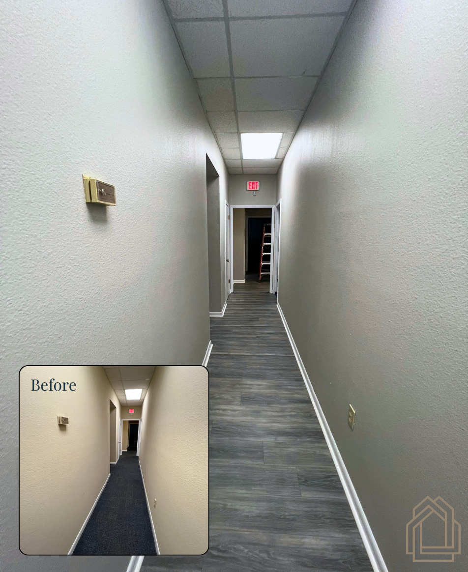 Narrow hallway with gray walls and carpet, ceiling tiles, and a lit exit sign at the end.