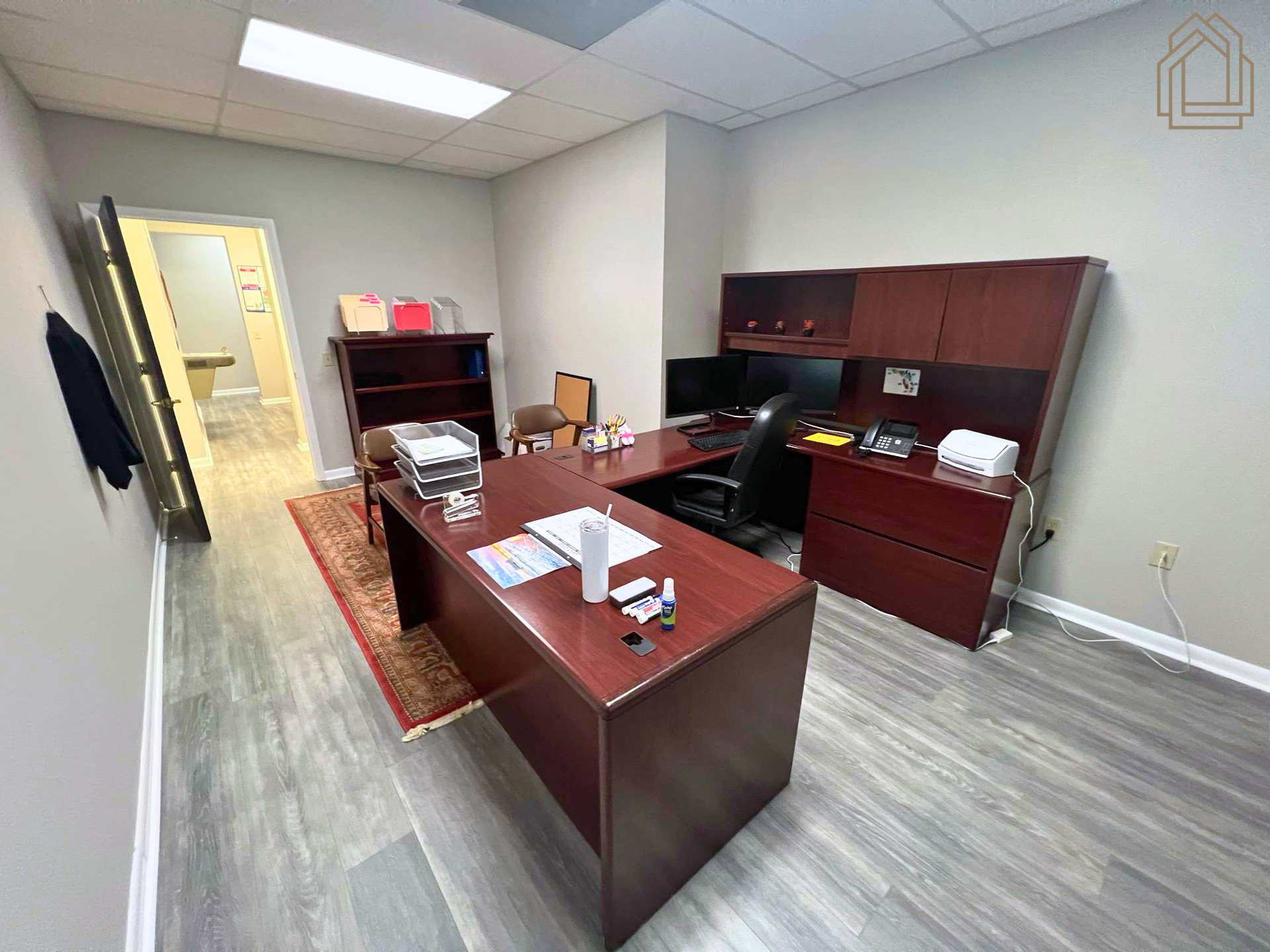Office with dark wood desk, matching cabinets, and a rug in a carpeted room with fluorescent lighting