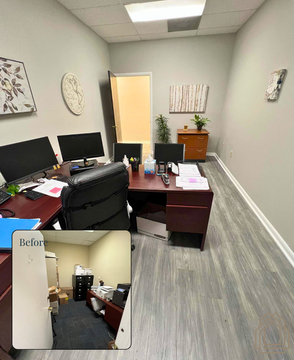Small office with desk, dual monitors, black chair, and cabinets; doorway and wall art in the background.