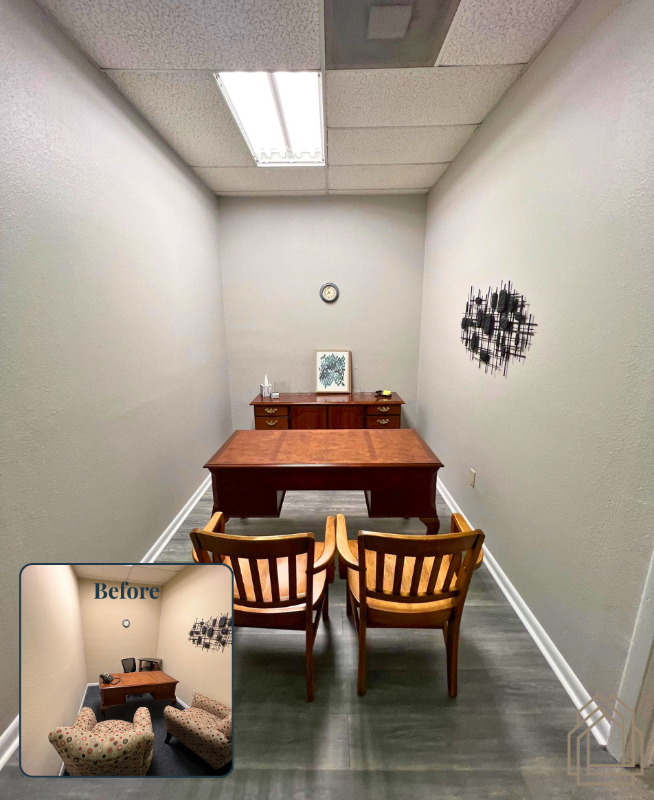 Small office with a wooden desk, two chairs, and wall decor in a narrow white room
