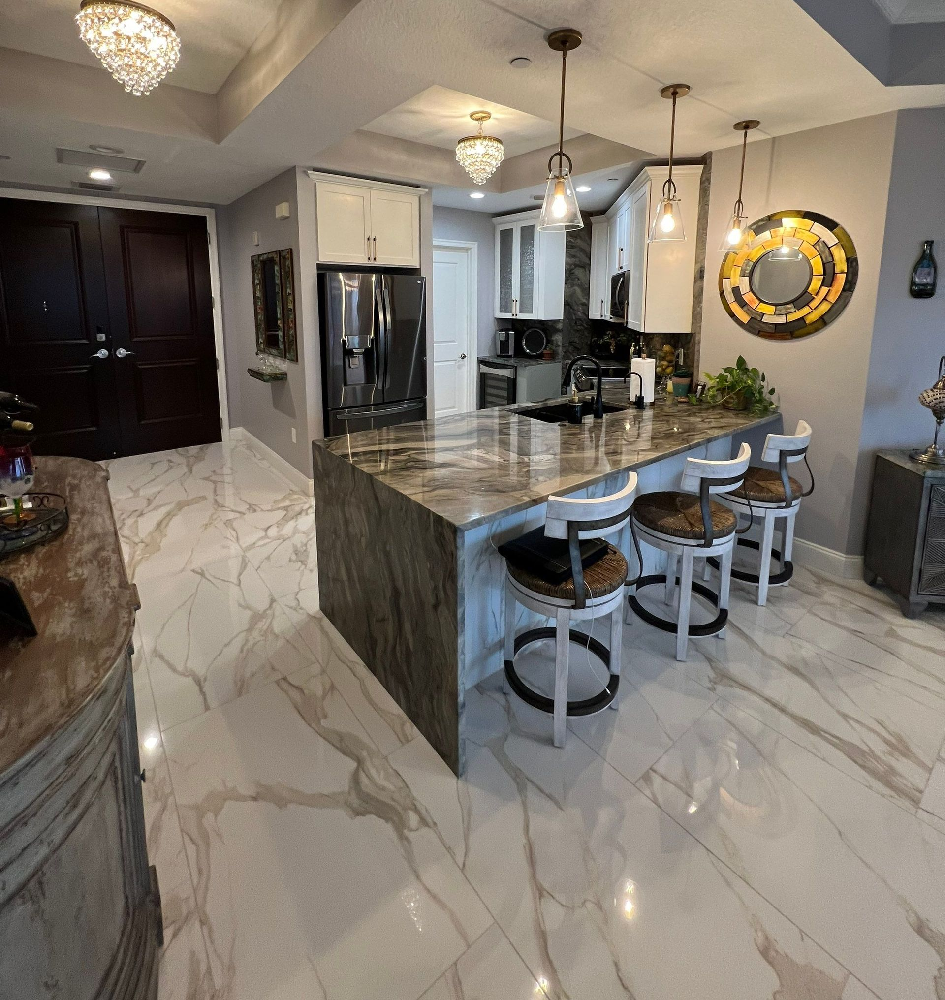Modern kitchen with marble floors, dark cabinets, stainless appliances, and a large island with bar stools