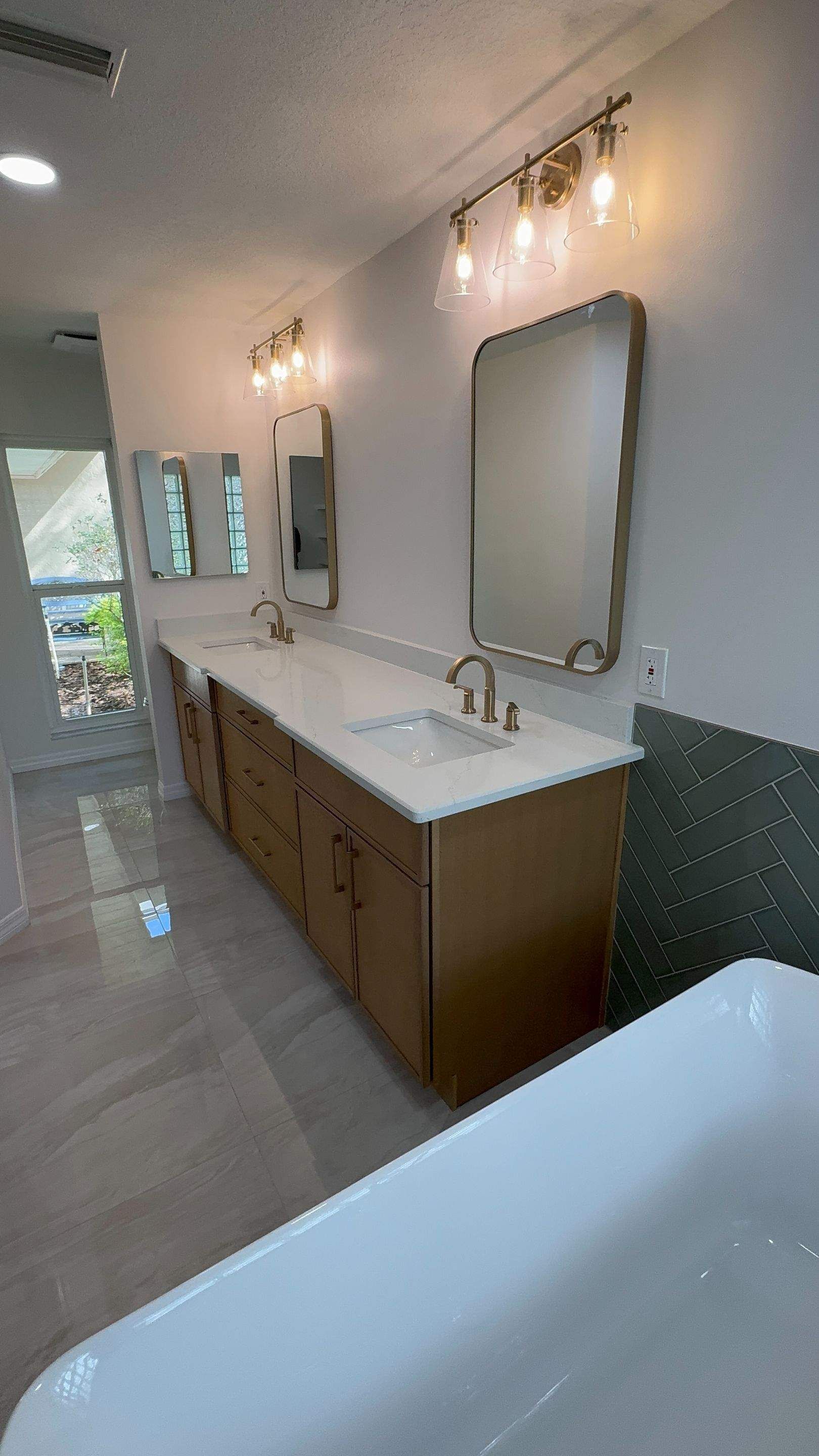 Long bathroom vanity with two sinks, mirrors, wall sconces, and a freestanding tub in the foreground.