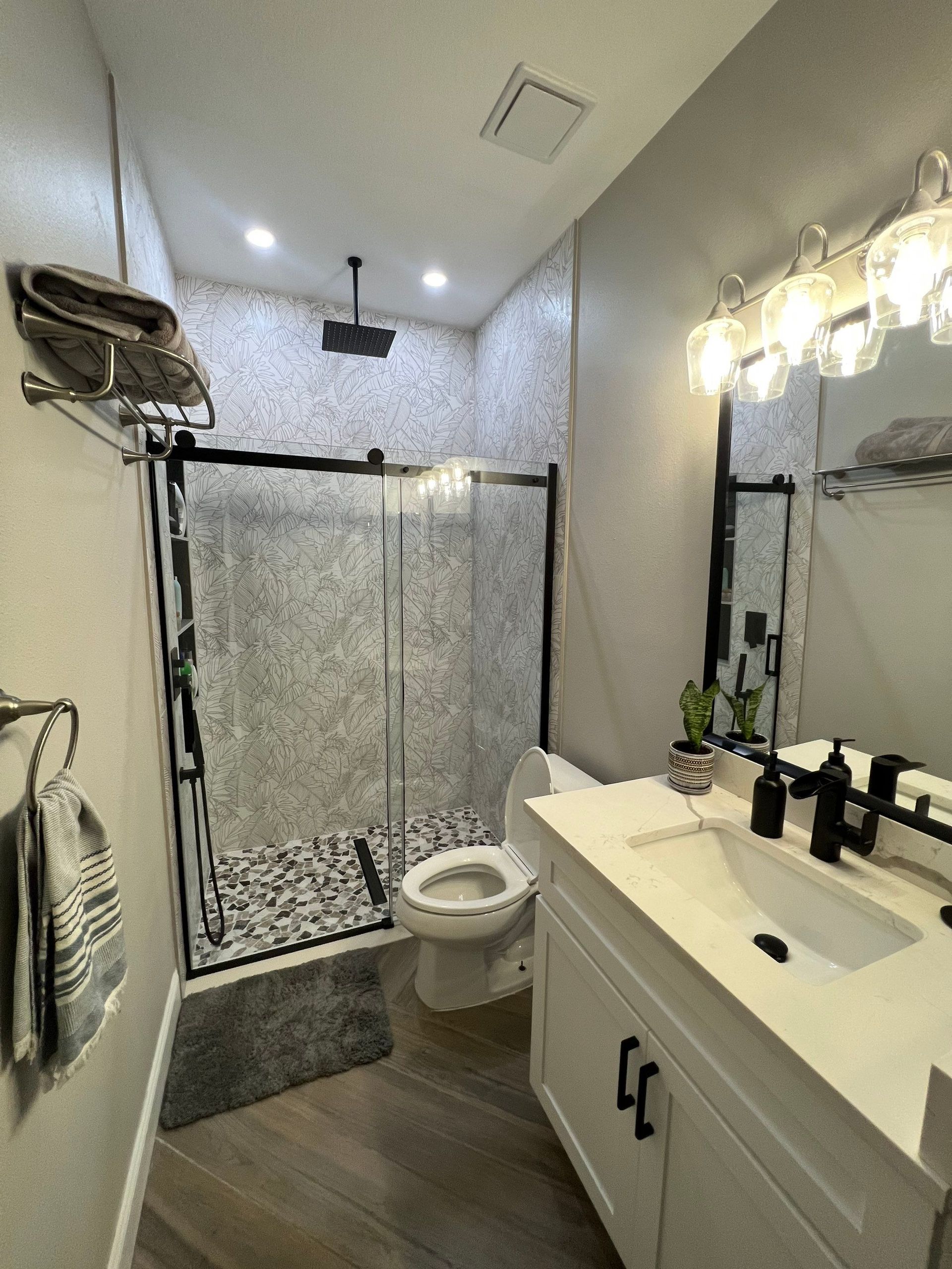 Bathroom with glass shower, toilet, and white vanity with mirror and lights.