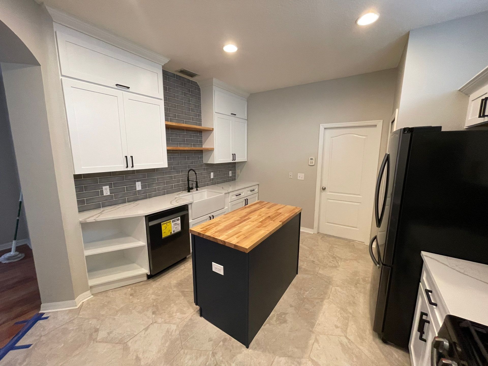 Bright modern kitchen with white cabinets, gray tile backsplash, island, and stainless steel appliances.