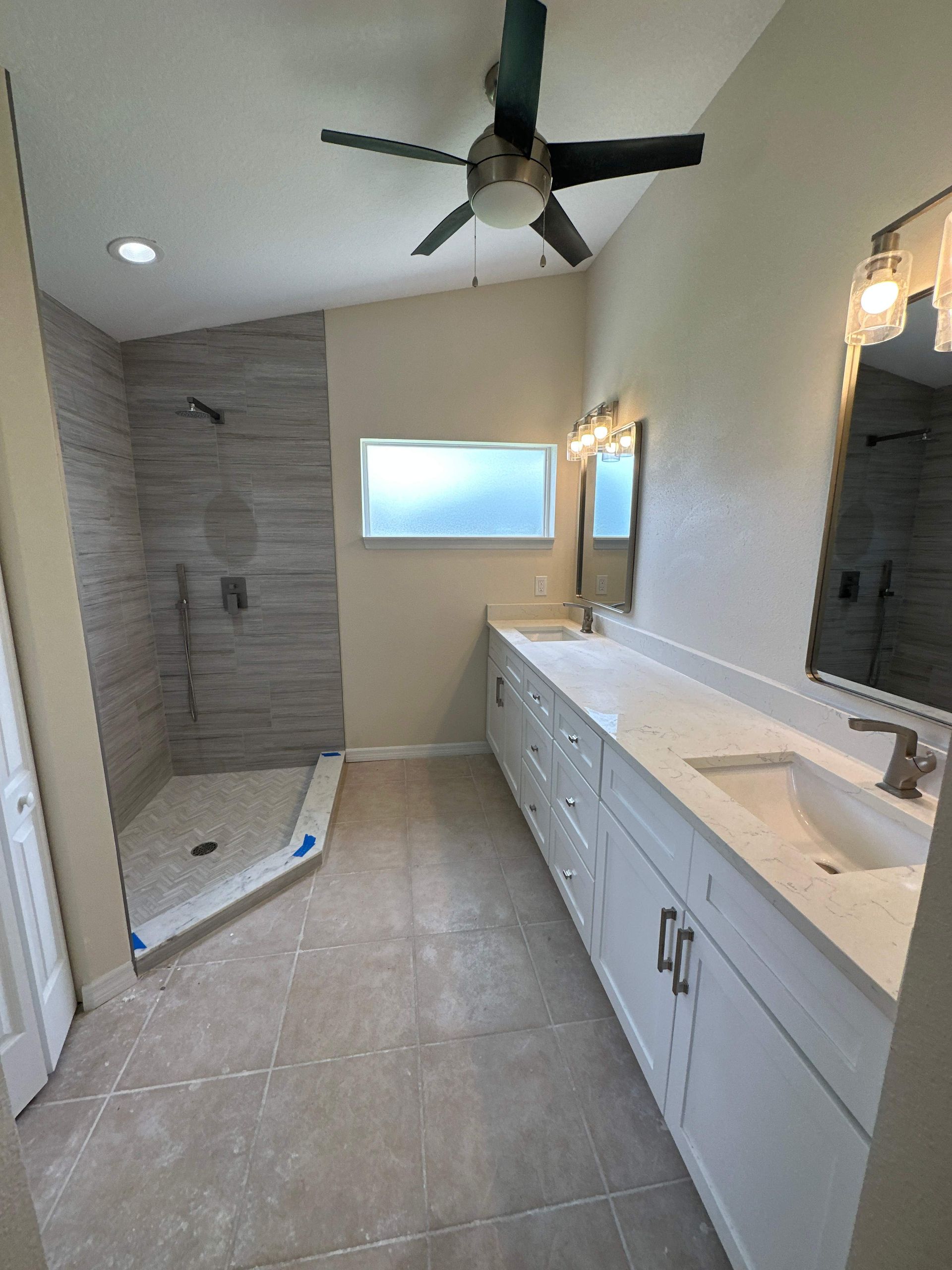 Modern bathroom with large vanity, walk-in shower, soaking tub, and ceiling fan, in light gray and white tones