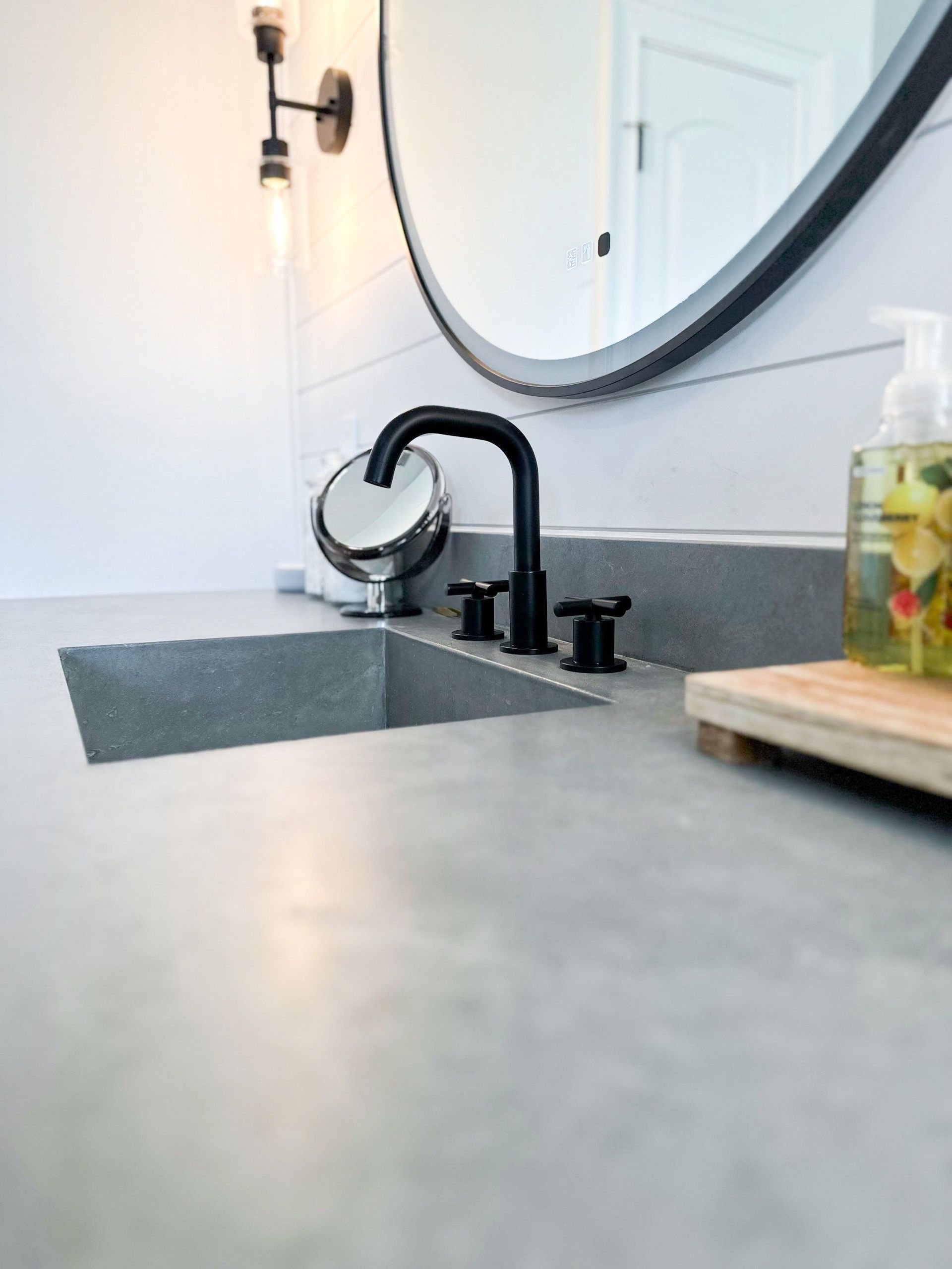 Modern bathroom sink with black faucet, round mirror, and soap dispenser on the counter