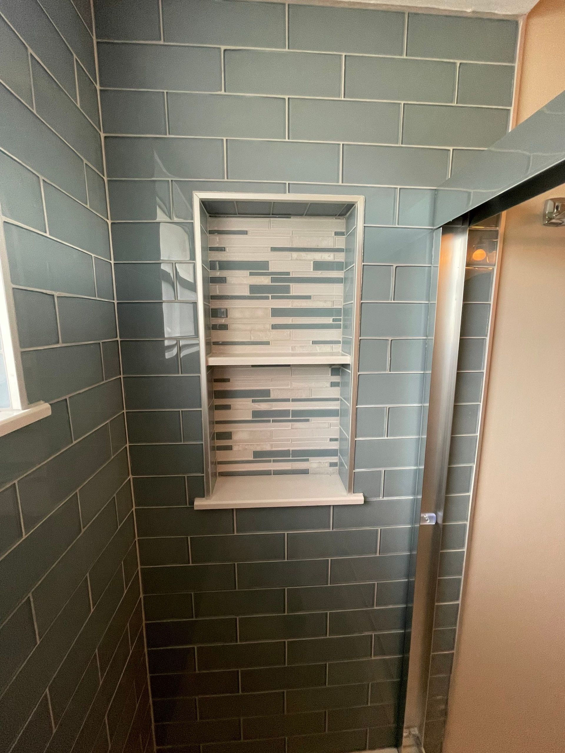 Small tiled shower with a narrow window and a glass door on the right.