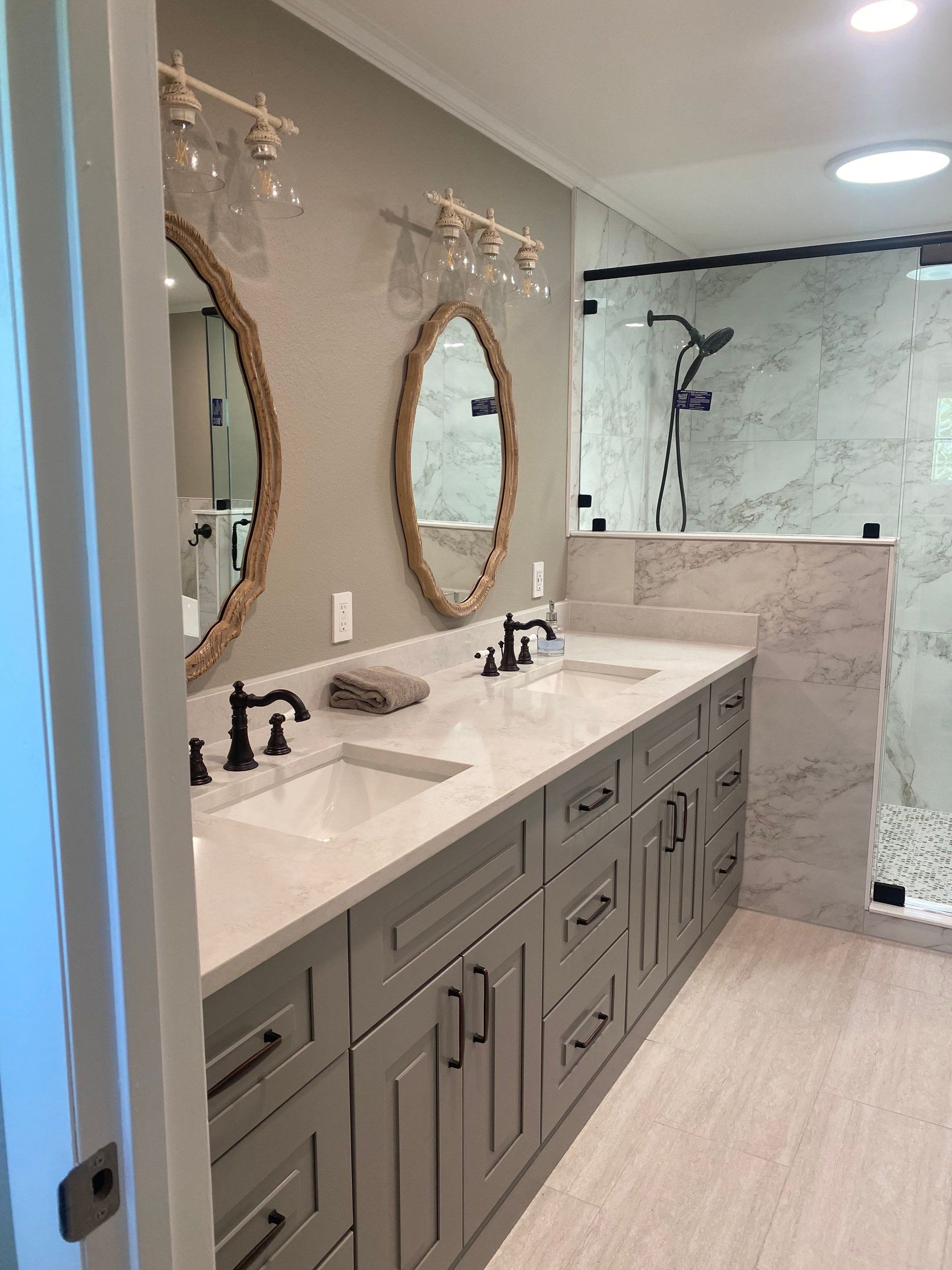 Modern bathroom with double vanity, oval mirrors, and a glass-enclosed shower.