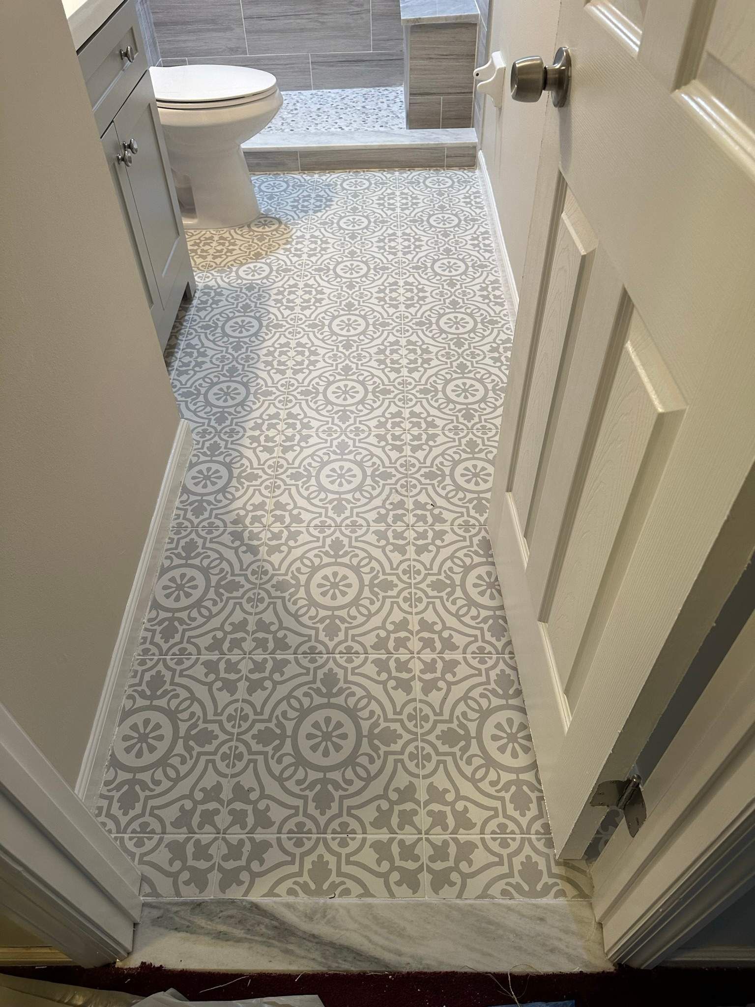Narrow bathroom hallway with gray patterned runner leading to a toilet and a blue bath mat.