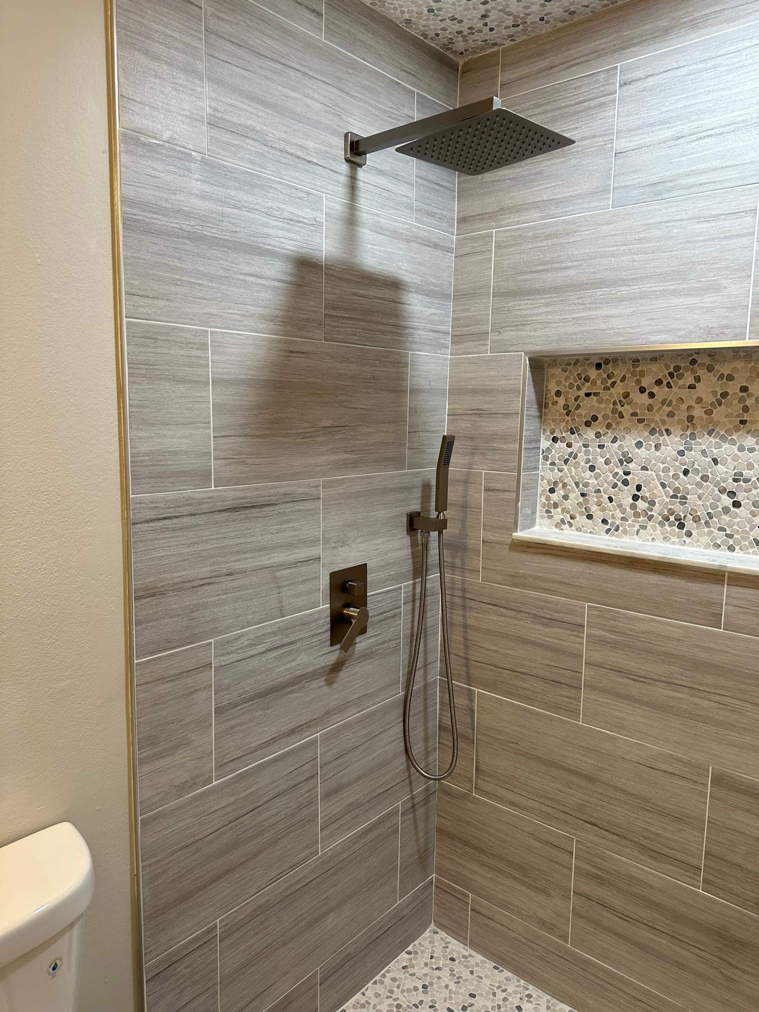 Modern tiled shower with rain showerhead, handheld sprayer, and recessed shelf