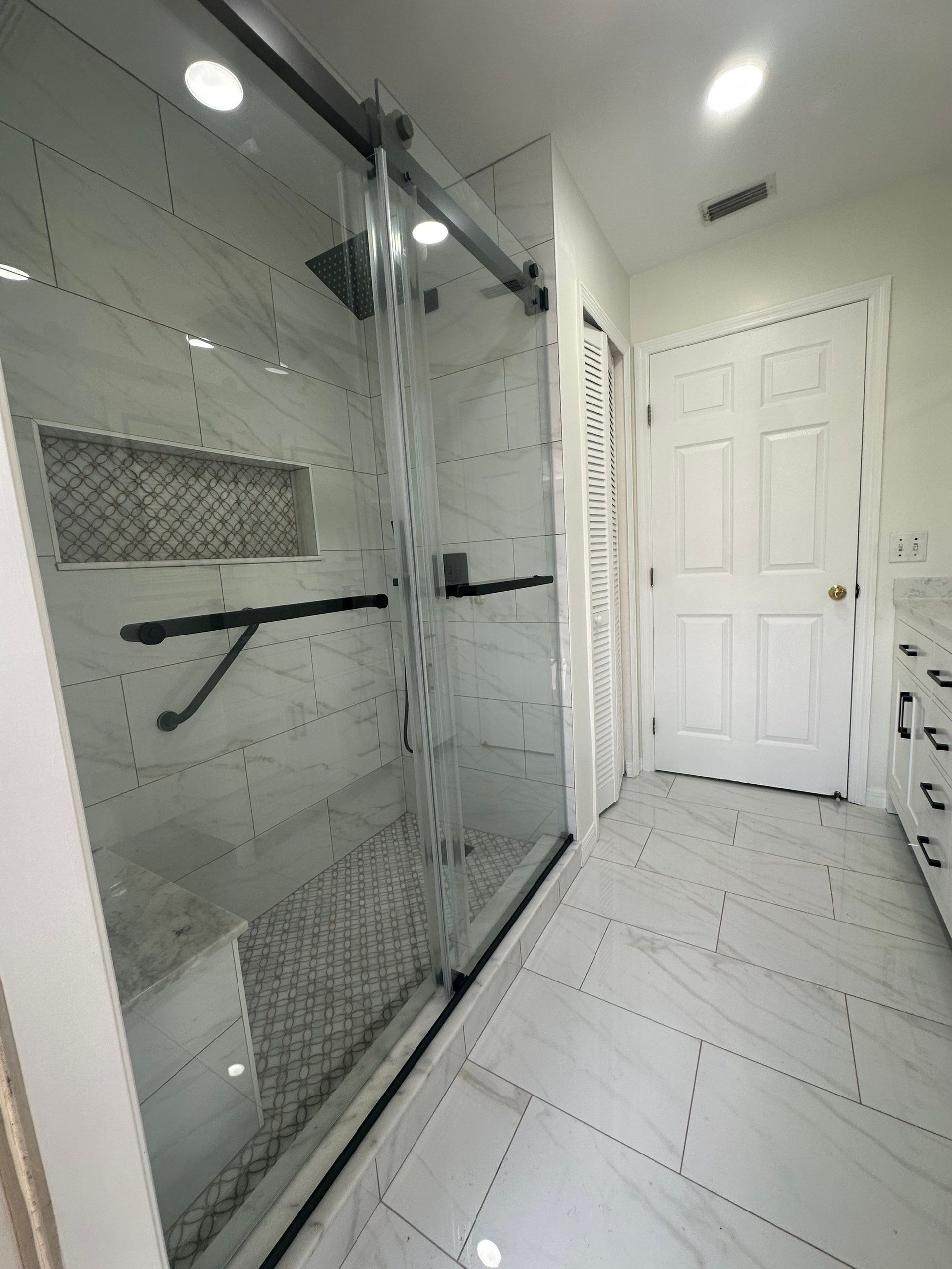 Modern bathroom with glass shower enclosure, white tile floor, and double doors in the background