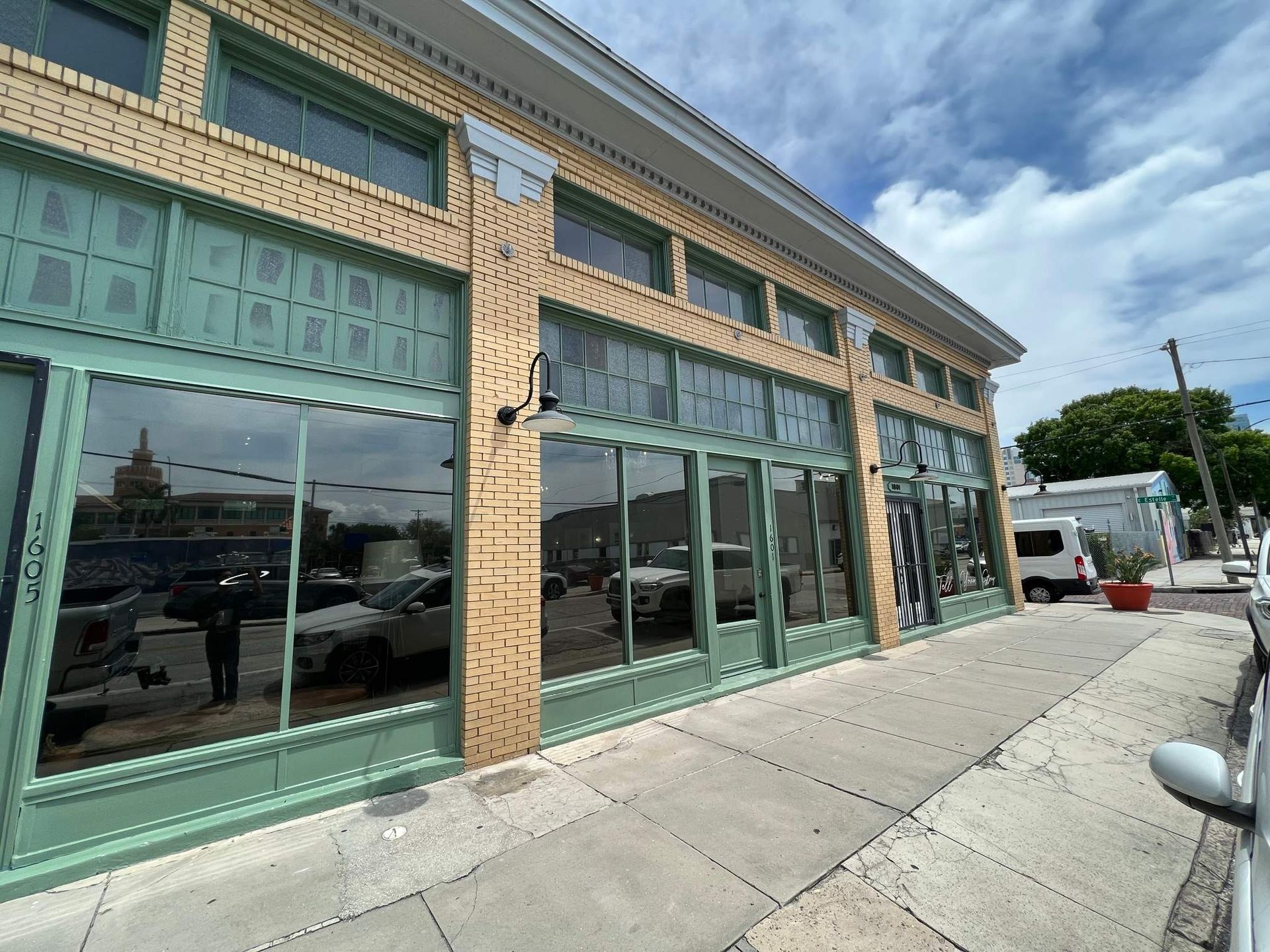 Green storefront with large windows and decorative trim on a sunny street corner