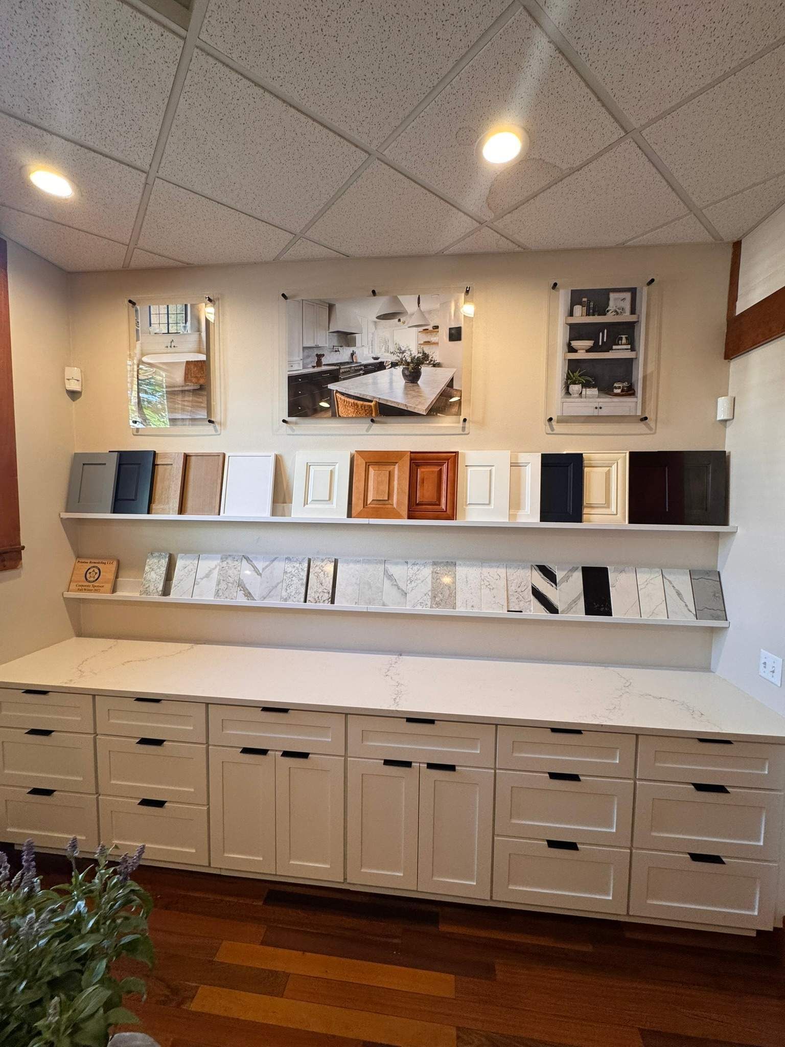 White wall display with framed art, shelves, and cabinets in a lobby or office reception area.