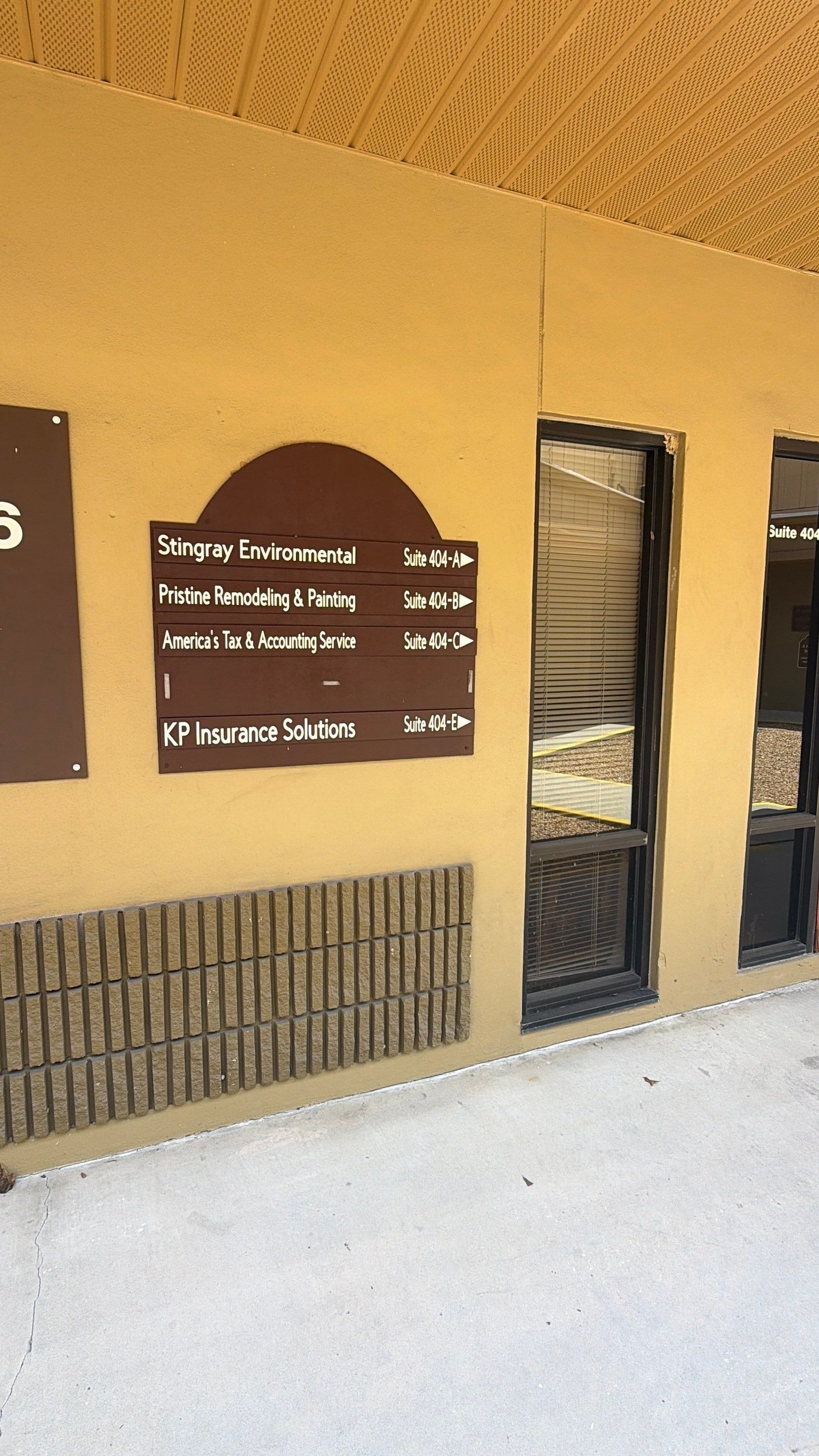Exterior of a tan building with a dark door, windows, and wall-mounted signs.