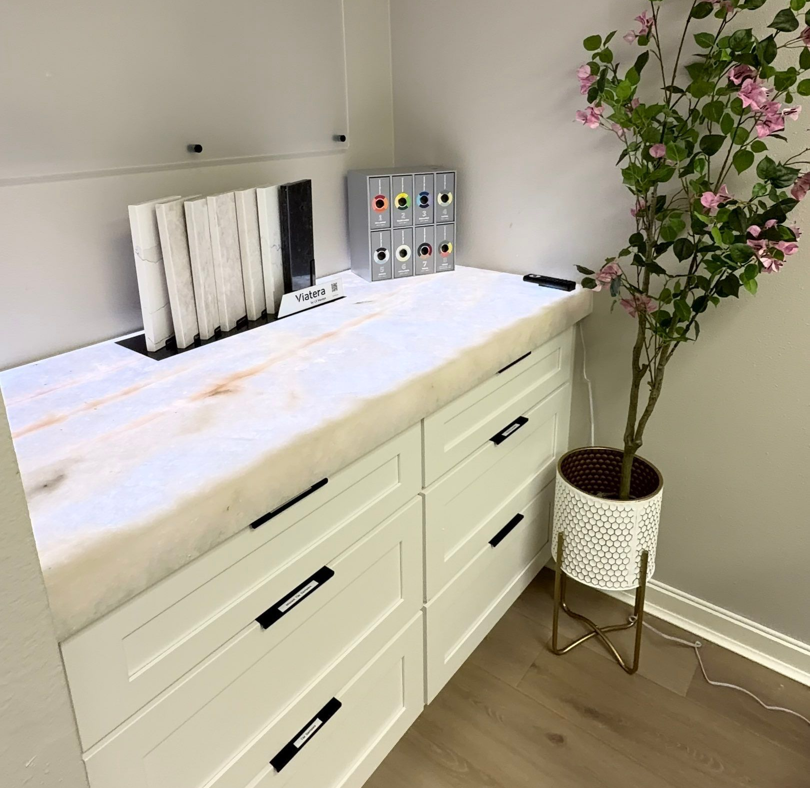 White cabinet with padded top, makeup organizers, and potted flowering plant in a bright room