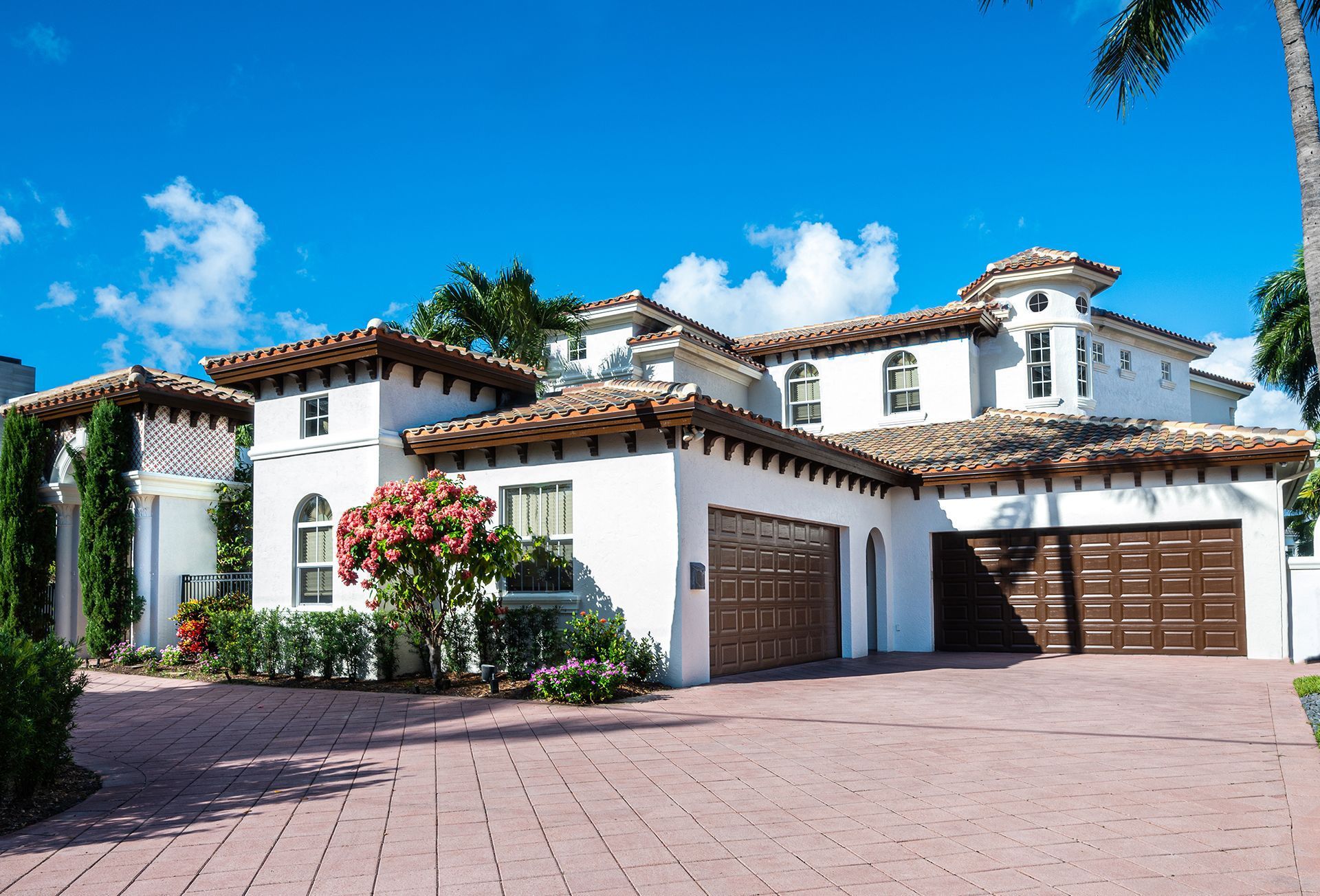 Large white Mediterranean-style house with red-tile roof, balconies, and a three-car garage under a blue sky