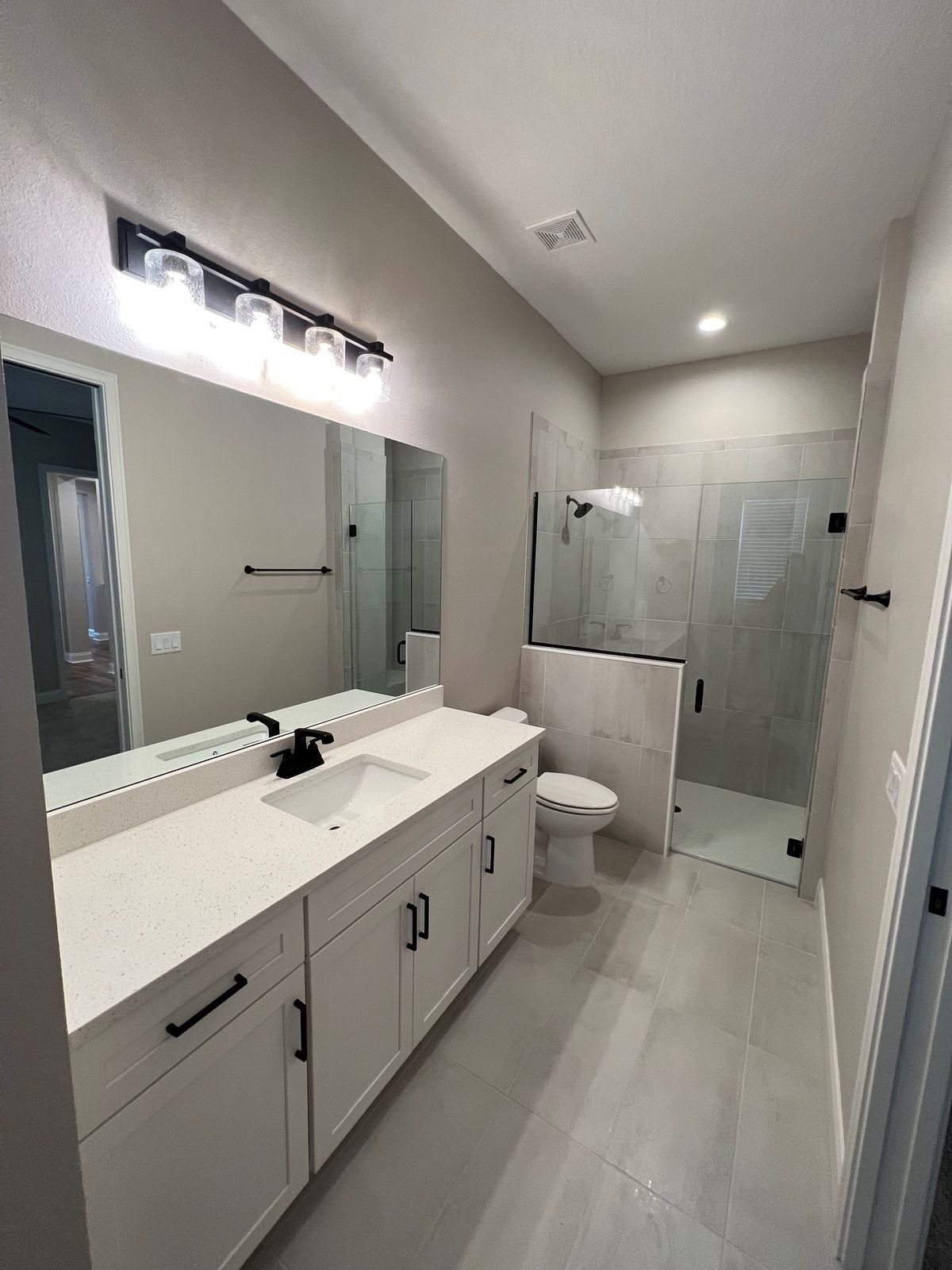 Modern bathroom with white vanity, large mirror, toilet, and glass walk-in shower.