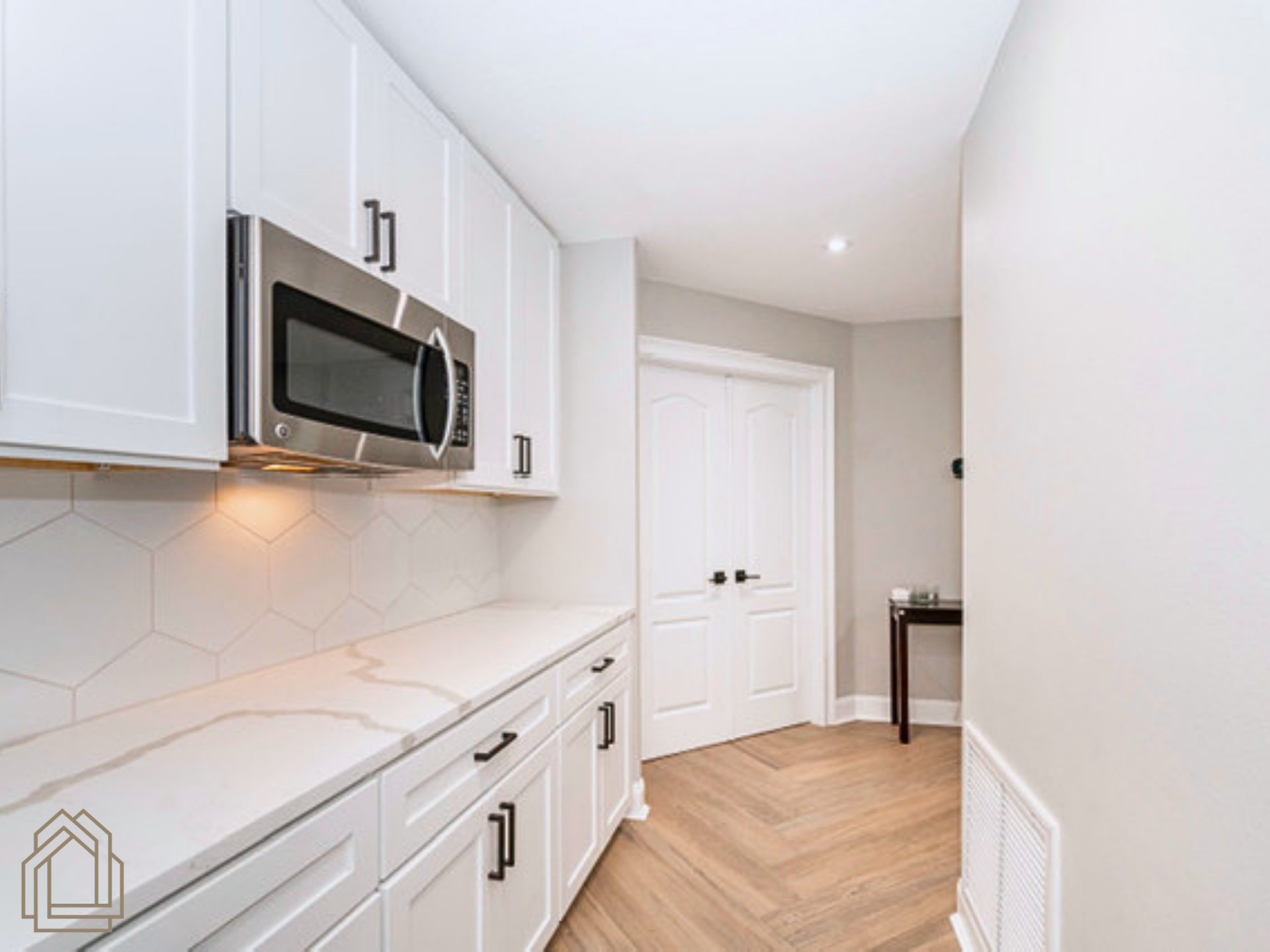 Bright modern kitchen with white cabinets, marble countertops, and stainless steel microwave.