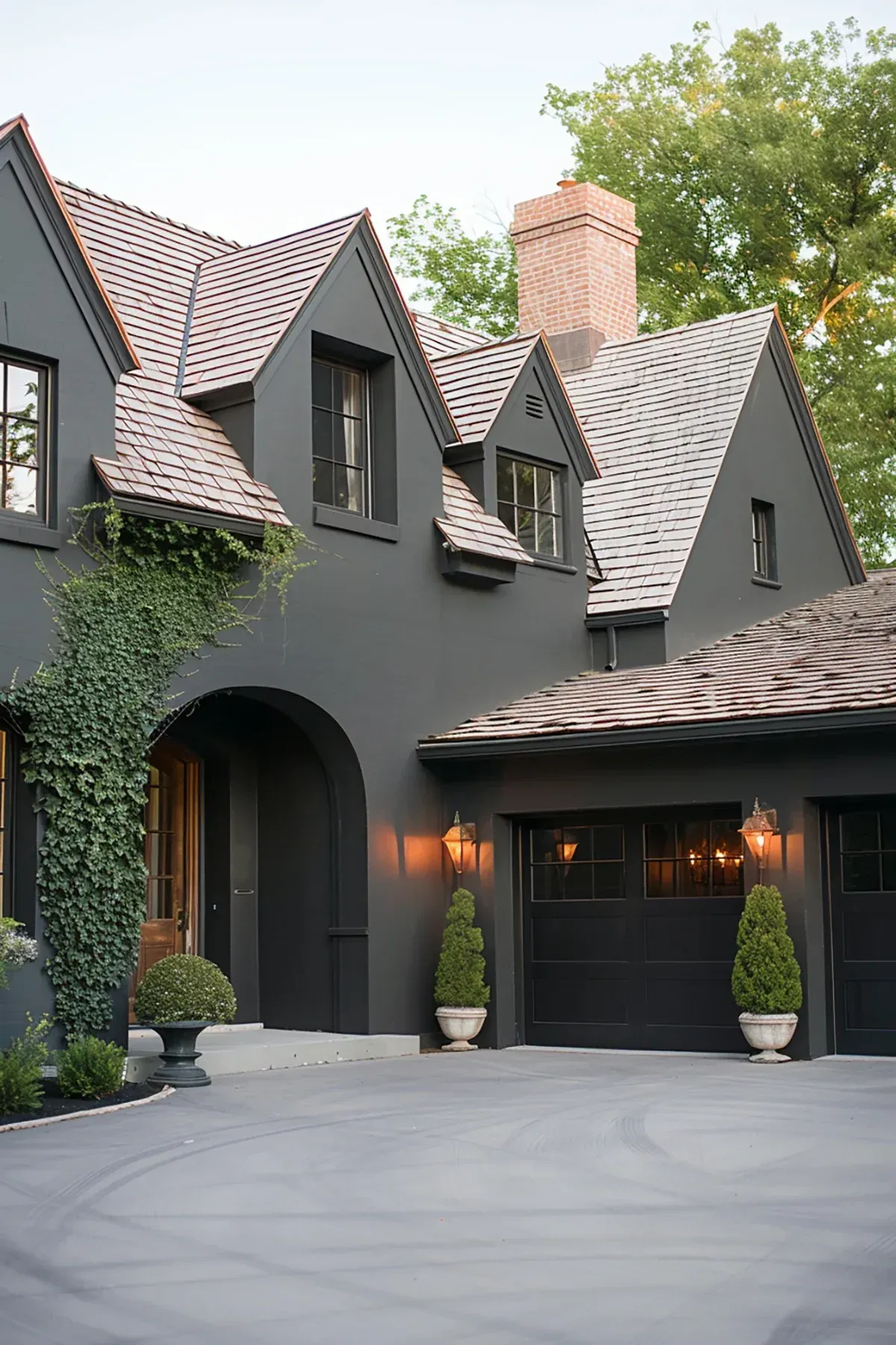 Dark gray modern house with steep gables, arched entry, garage, and a large paved driveway.