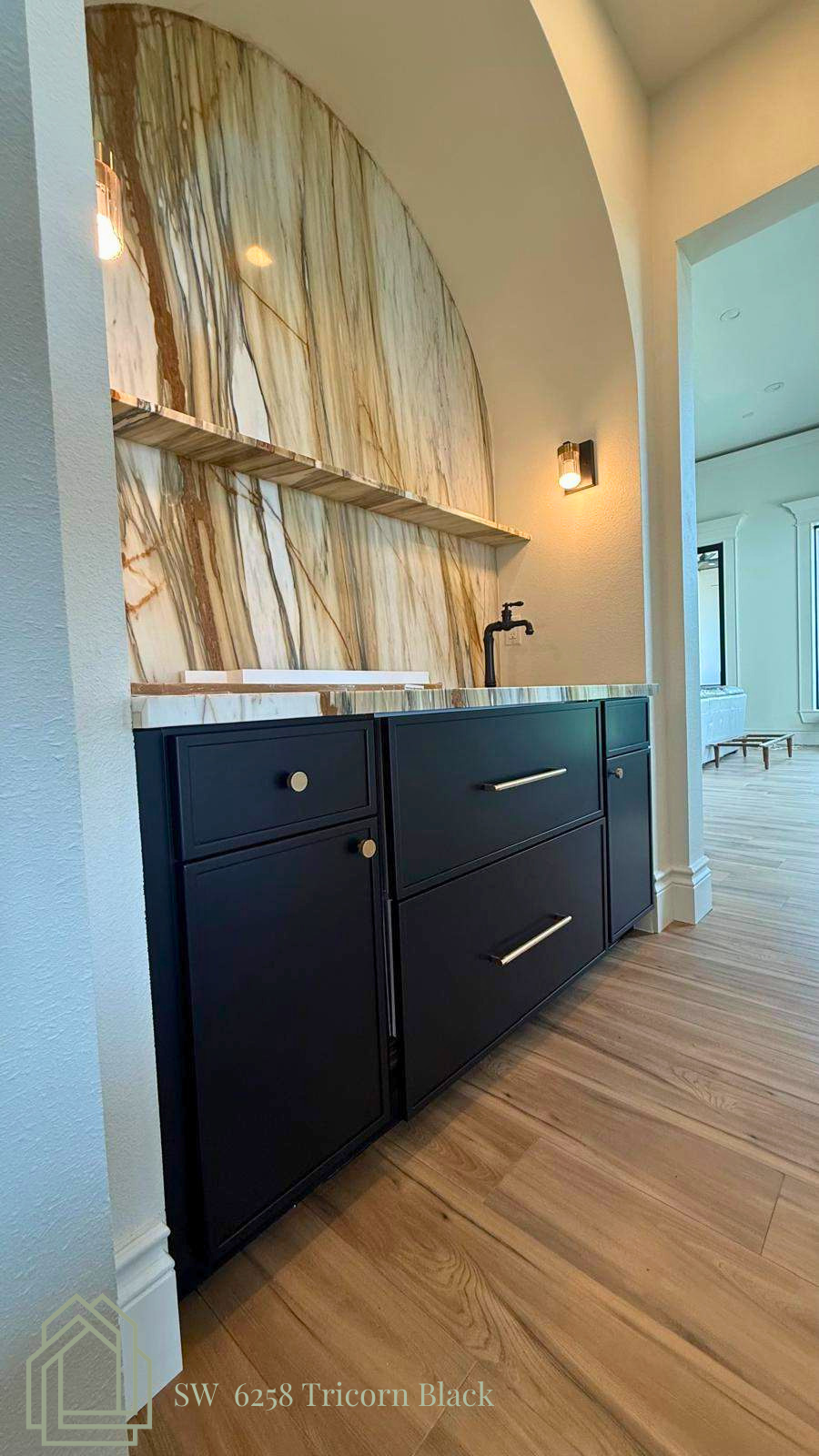 Modern bathroom vanity with dark cabinets, brass mirror, and large arched wall opening