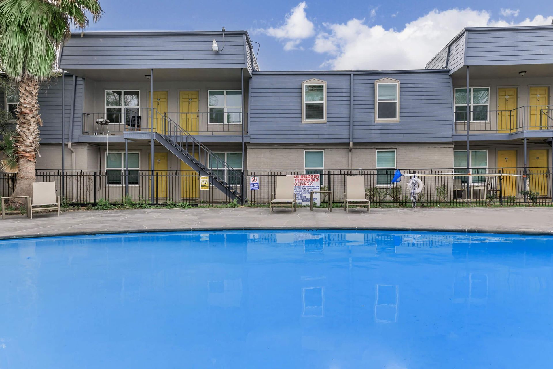 Outdoor pool in front of a two-story apartment building with yellow doors