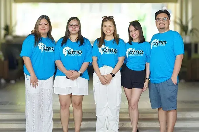 Five people in matching blue T-shirts standing indoors and smiling at the camera