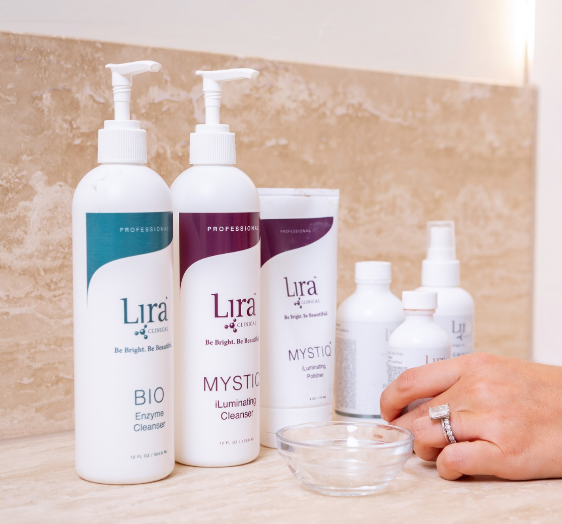 Lira skincare bottles and jars on a counter beside a hand with a ring and a small glass bowl