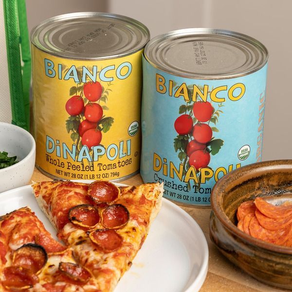 Two BIANCO Dinapoli tomato cans beside pizza slices and bowls of sauce on a table.