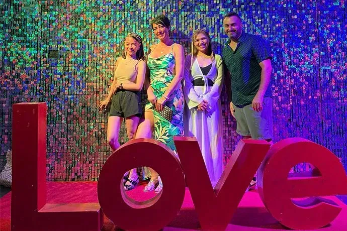 Four people posing behind a large red “Love” sign against a colorful mosaic wall.