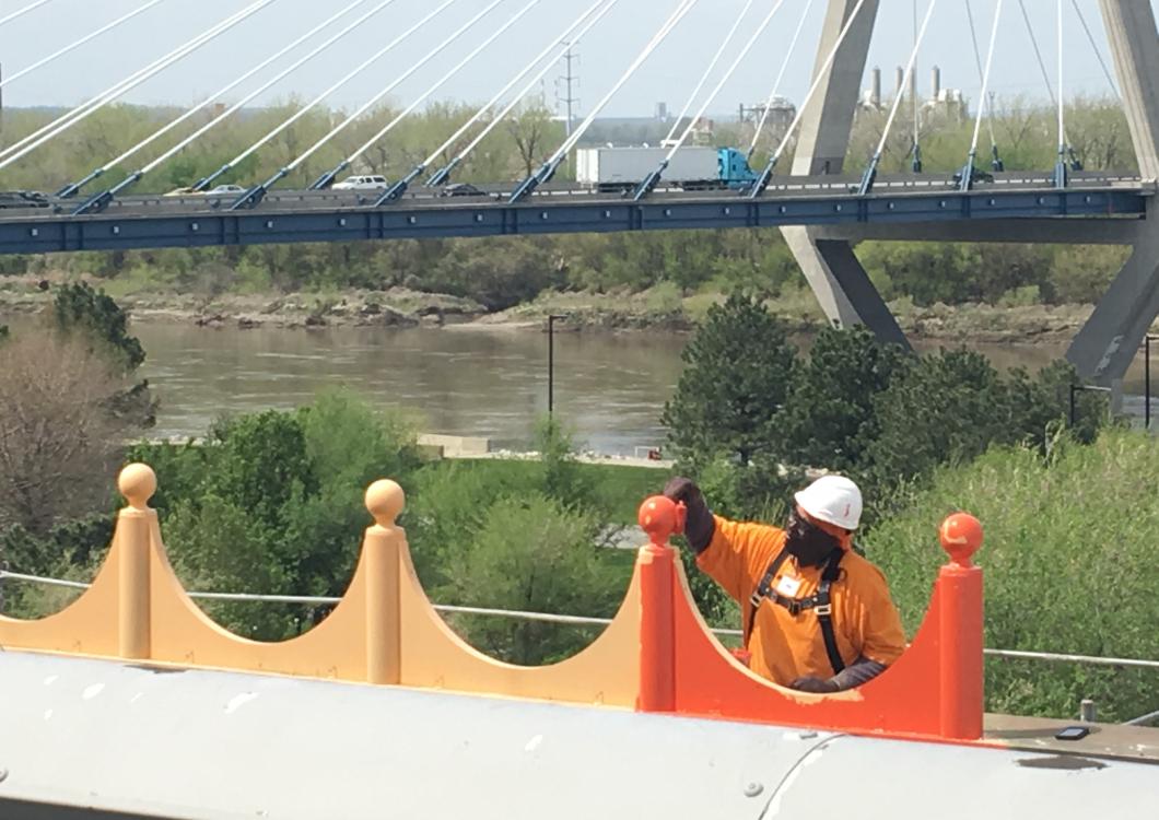 Person in an orange jacket and white helmet near a river bridge with cable supports