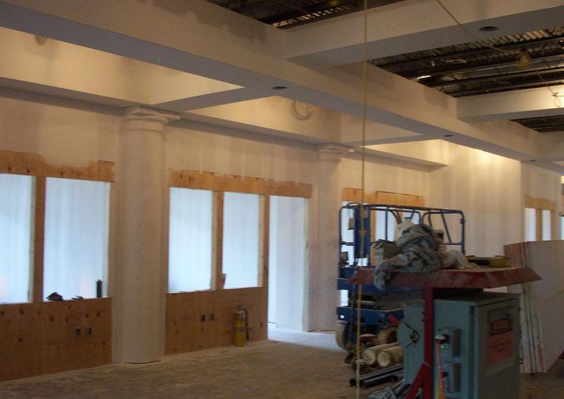 Partially finished room with white walls, exposed ceiling beams, and construction materials near windows