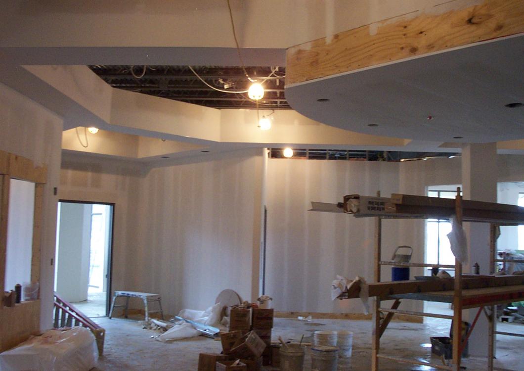 Interior of a room under construction with drywall, exposed ceiling beams, and scaffolding