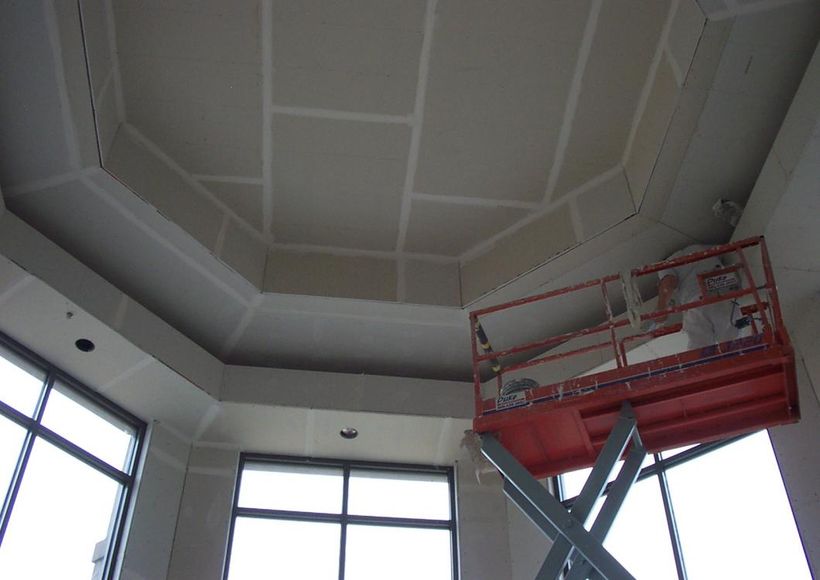 Interior ceiling with octagonal paneling and a red construction lift near tall windows