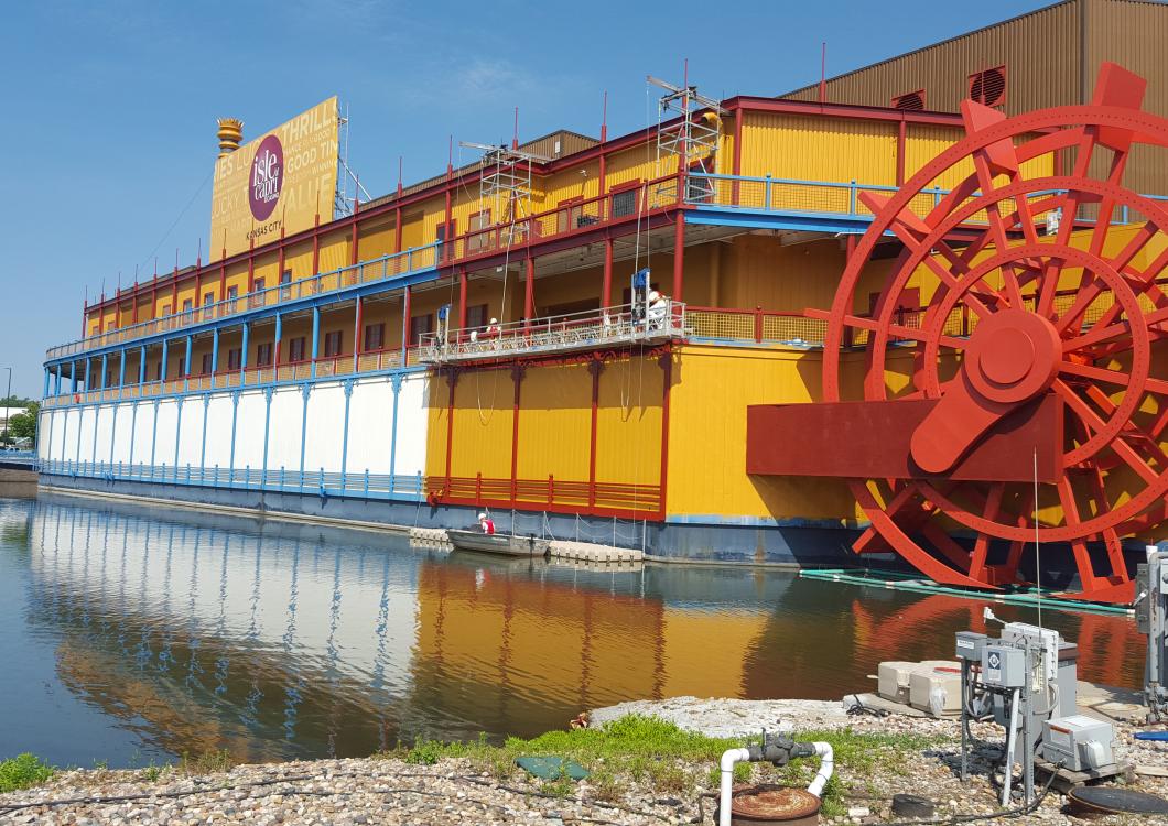 Large colorful riverboat with a red paddle wheel docked on calm water under a clear sky