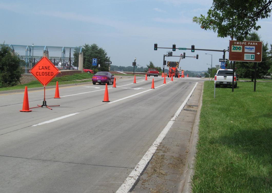 Road construction zone with orange cones and flagger signs blocking lanes on a highway