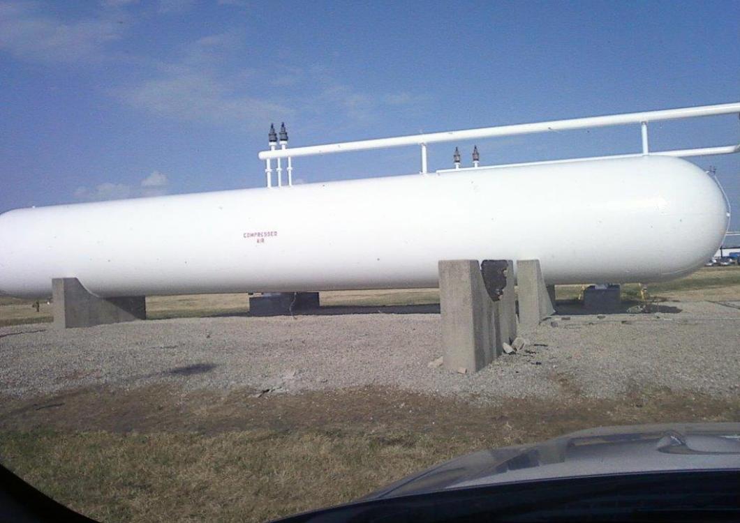 White horizontal cylindrical tank on concrete supports in a grassy field under a blue sky