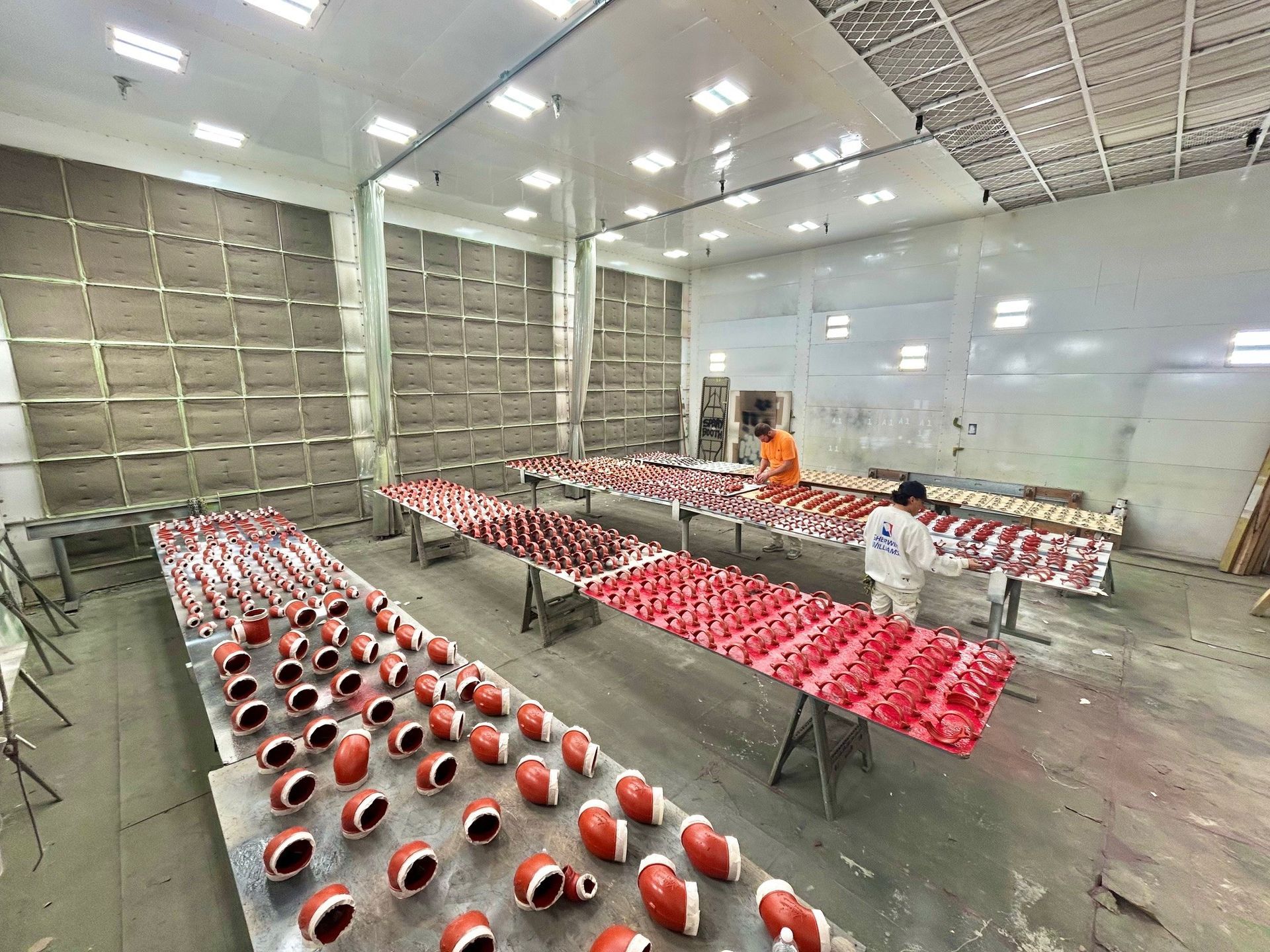 Workers inspecting rows of red-and-white helmets on tables in a large industrial room