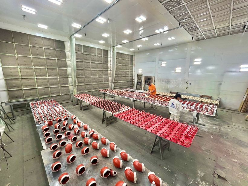 Rows of red-and-white helmets on tables in a large industrial room, with two workers in the background