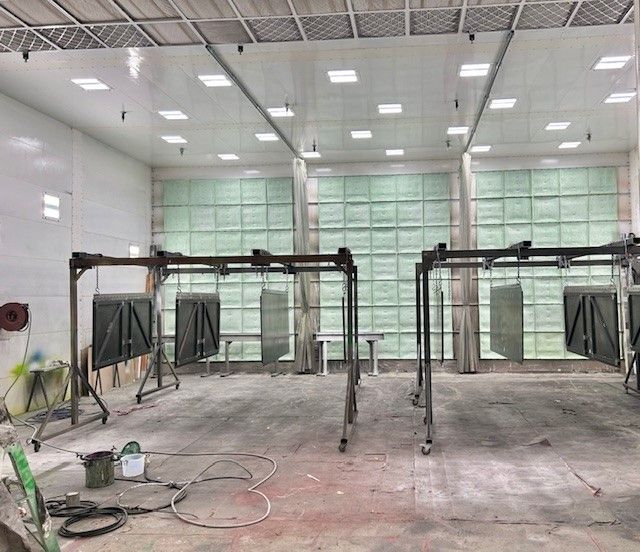 Industrial spray booth with metal frames, hanging panels, and a concrete floor under bright ceiling lights