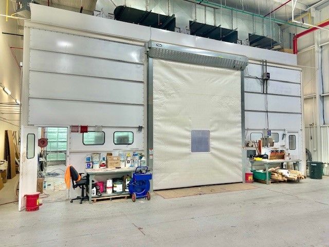 Industrial warehouse interior with a large roll-up door, workbench, and storage items.