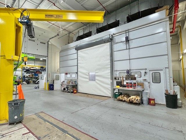 Industrial workshop with a large gray sliding door, yellow crane overhead, and tools along the wall