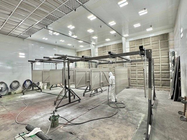 Metal spray booth with hanging frames and hoses in a white industrial workshop