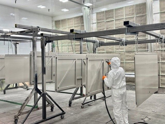 Person in white protective suit spraying metal frames in an industrial workshop